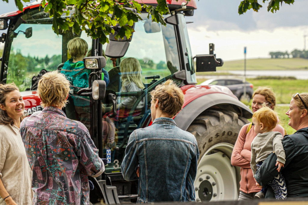 Voksne står og taler, mens deres børn leger på en traktor